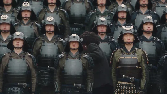 A curly-haired lead stands among synchronized samurai